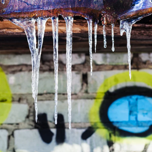 Eiszapfen auf rostigem Hausdach mit Ziegelmauer — Stockfoto