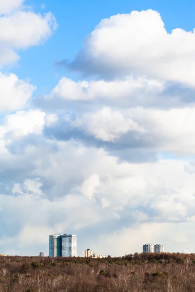 Cumulus clouds in sky over buildings and woods — Stock Photo, Image