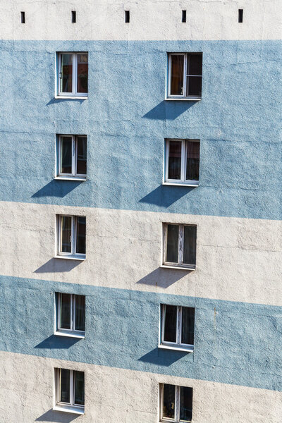 Concrete wall of residential urban high-rise building with windows illuminated by sun