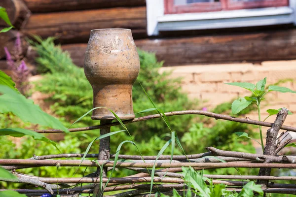 Wattle fence with old clay pot and log house — Stock Photo, Image