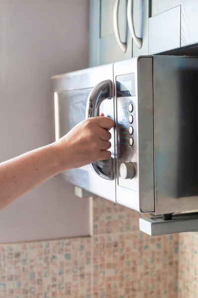 Mão fecha forno de microondas para aquecimento de alimentos — Fotografia de Stock
