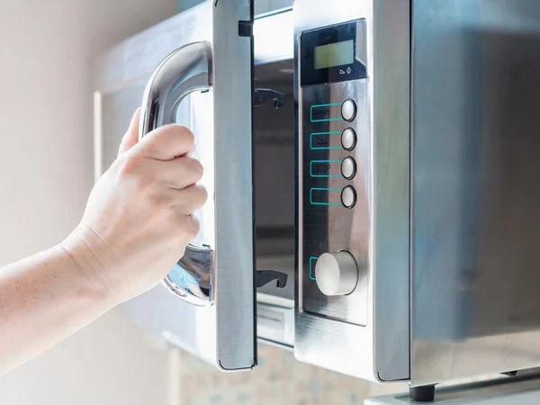 Hand opens microwave oven for cooking food — Stock Photo, Image