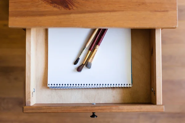 Painting brushes on drawing album in open drawer — Stock Photo, Image
