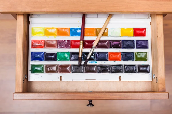 Box with watercolor paints and brushes in drawer — Stock Photo, Image