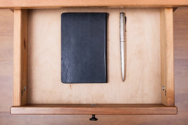 Silberner Stift und schwarzes Notizbuch in offener Schublade — Stockfoto