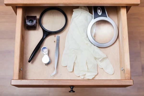 Förstoringsglas, pincett och handskar i öppna kassalådan — Stockfoto