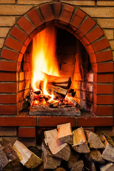 Woods pile and burning firewood in brick fireplace — Stock Photo, Image