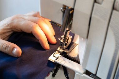 Terzi, kumaşın kenarını serger 'a diker. Evinde yakın çekim yapar.