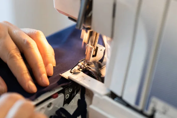seamstress processes the edge of fabric on household overlocker close up at home