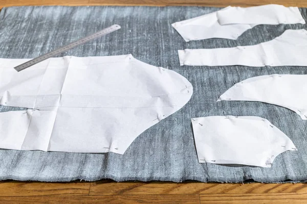 Paper sewing pattern layouts of dress and steel ruler on gray fabric on wooden table at home — Stock Image Paper Sewing Pattern Layouts Dress Steel Ruler Gray Fabric Wooden Royalty Free Stock Images