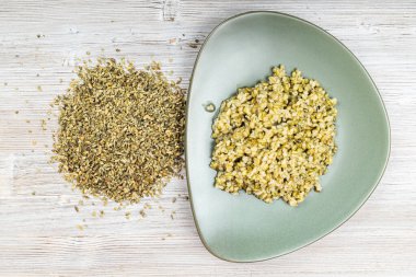 Ham freekeh buğday taneleri ve ahşap masada yeşil tabakta haşlanmış yulaf lapası.