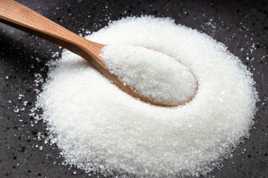 Beyaz rafine pancar şekerli ahşap kaşık siyah seramik tabağa yakın.