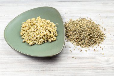 ham freekeh buğday taneleri ve kaynamış yulaf lapası ahşap masada yeşil tabakta