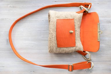 top view of open hand-knitted casual cross body bag with orange leather cover on gray wooden table