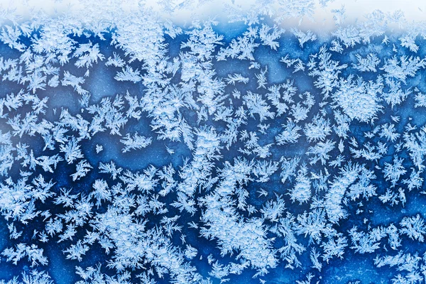 Snowflakes and blue frost on glass in winter — Stock Photo, Image