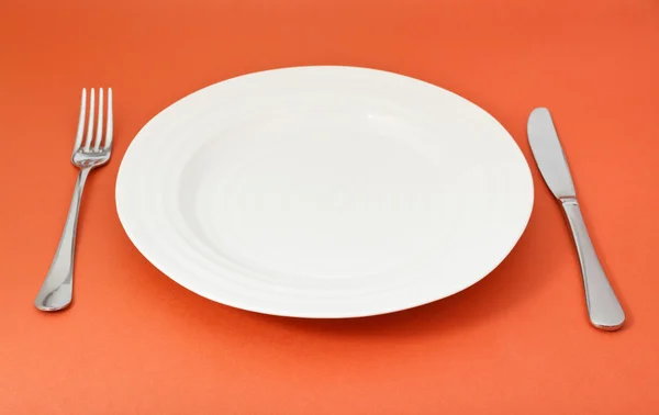 Empty white plate with fork and knife set on red — Stock Photo, Image