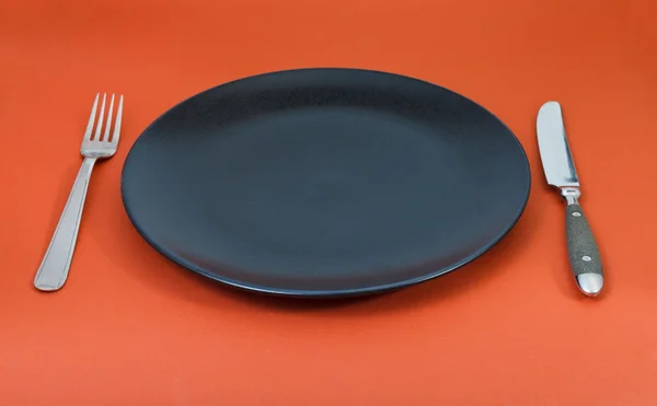 Empty black plate with fork and knife set on red — Stock Photo, Image