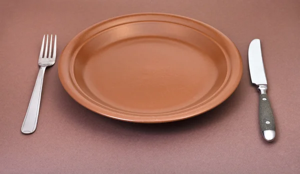 Prázdný talíř hnědý s vidličkou a nožem na hnědé — Stock fotografie