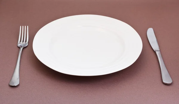 Empty white plate with fork and knife on brown — Stock Photo, Image