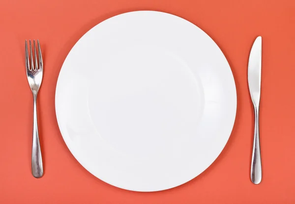 Top view of porcelain plate, fork, knife on red — Stock Photo, Image
