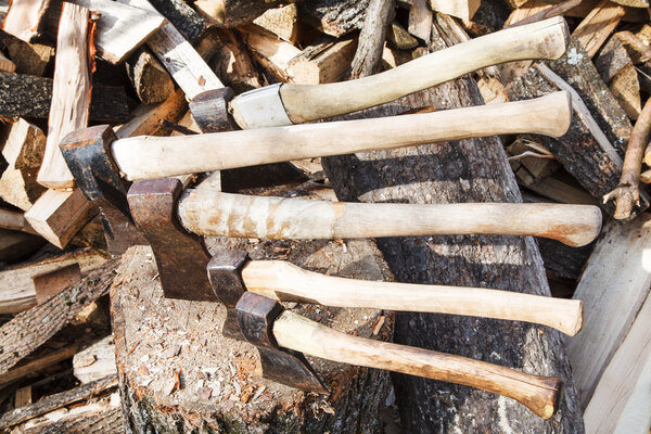 axes in wood block near stack of firewoods