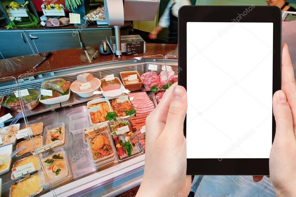 Travel concept - tourist photograph meat and delicacies in in small butcher shop in France on tablet pc with cut out screen with blank place for advertising logo