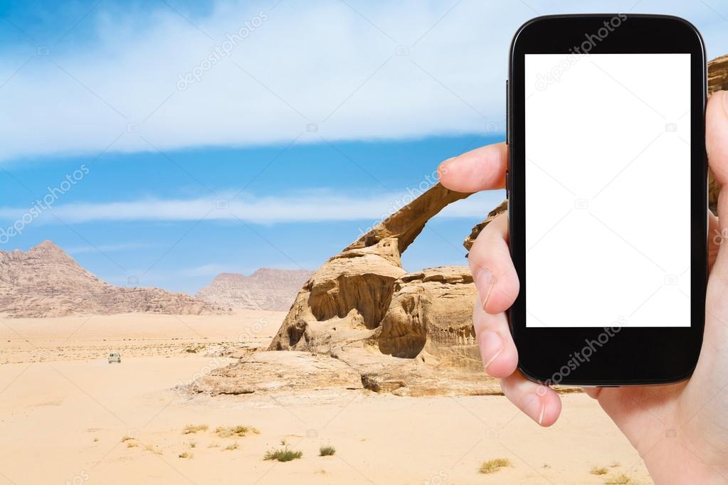 Travel concept - tourist photograph Bridge rock in Wadi Rum desert, Jordan on smartphone with cut out screen with blank place for advertising logo