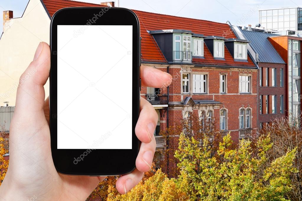 Travel concept - tourist photograph brick facade of residential building of 19th century in Berlin in autumn morning on smartphone with cut out screen with blank place for advertising logo