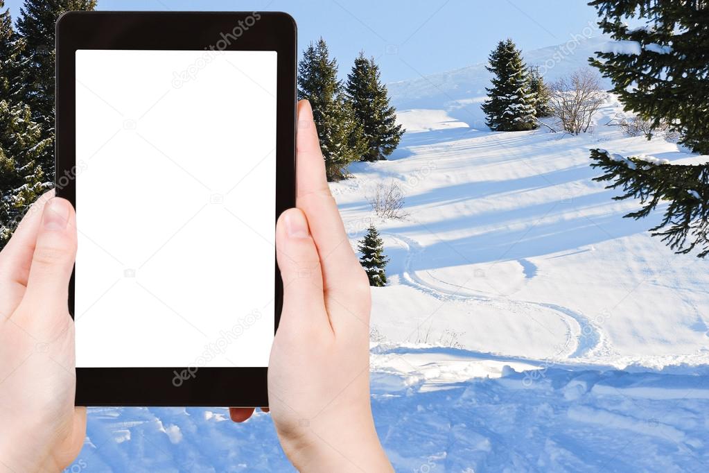 Travel concept - tourist photograph skiing tracks in snow forest on mountain in Portes du Soleil region, Morzine - Avoriaz, France on tablet pc with cutout screen with blank place for advertising logo