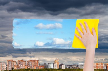 hand deletes dark clouds over city by yellow cloth clipart
