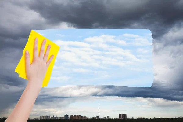Рука удаляет дождливое облако над городом желтой тканью — стоковое фото