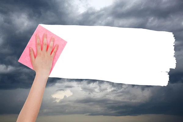 Hand deletes dark rain clouds on sky by pink rag — Zdjęcie stockowe