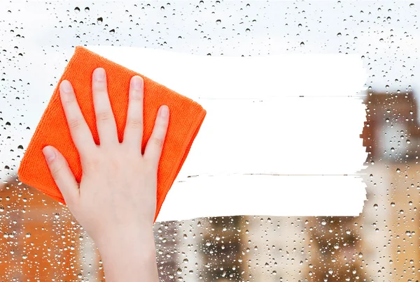 Hand deletes rain drops on window by orange rag — Stockfoto