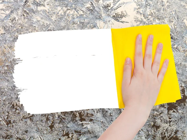 Hand deletes frozen pattern on glass by yellow rag — Zdjęcie stockowe