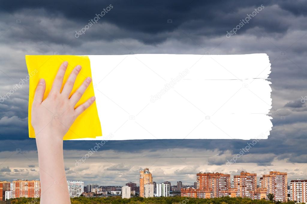 hand deletes rainy clouds over urban houses by rag