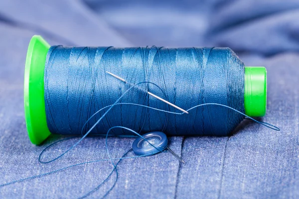 Thread bobbin with needle, button on blue jacket — Stock Photo, Image