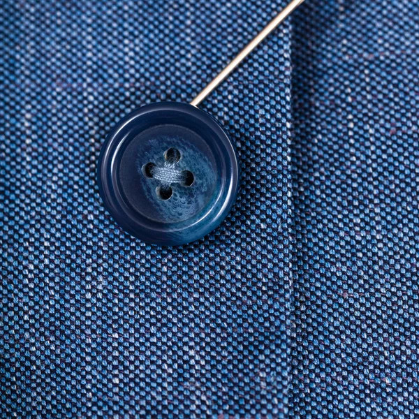 Прикрепление пуговицы к синей шелковой ткани по игле — стоковое фото