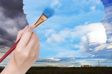 paintbrush paints blue sky on rainy clouds