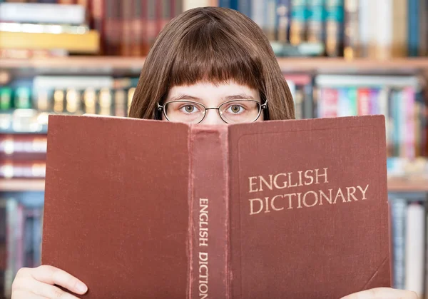 Girl looks over Dicionário Inglês na biblioteca — Fotografia de Stock