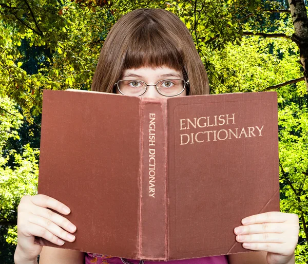 Menina olha sobre Dicionário Inglês e madeiras verdes — Fotografia de Stock