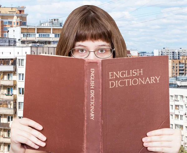Девочка смотрит на английский словарь и город — стоковое фото