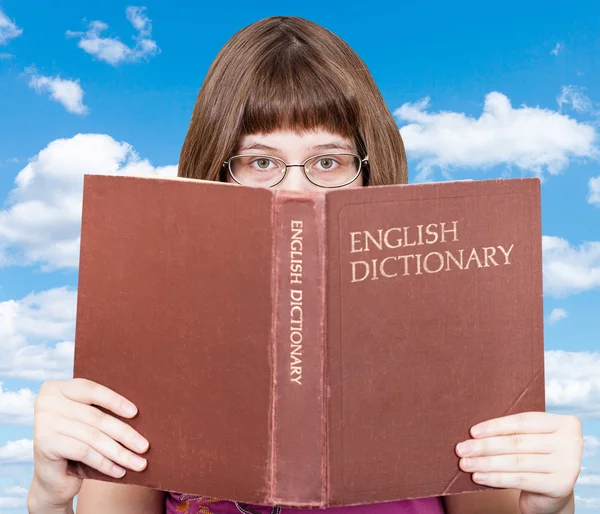 Meisje kijkt over English Dictionary en blauwe hemel — Stockfoto