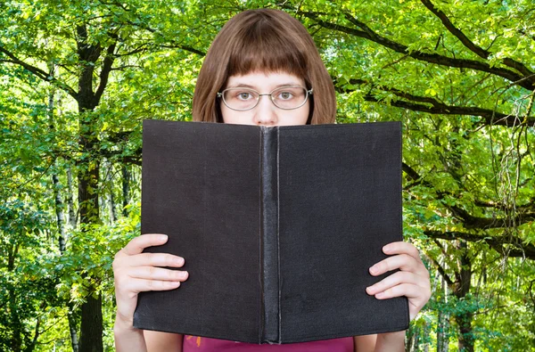 Chica lee libro grande y verde bosque de verano —  Fotos de Stock