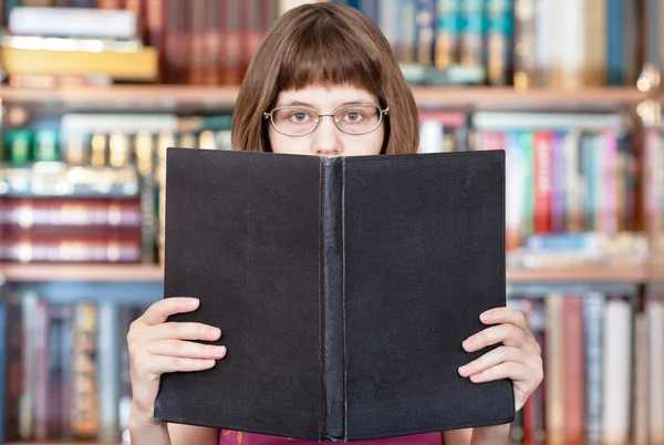 Chica lee libro grande y libros estantes —  Fotos de Stock