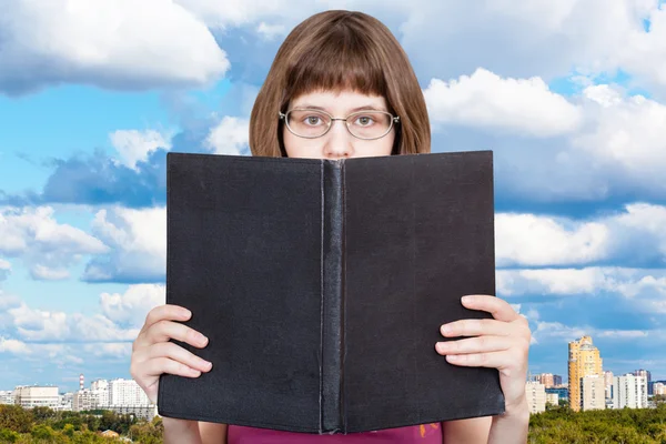 Chica lee gran libro y nubes azules sobre la ciudad —  Fotos de Stock