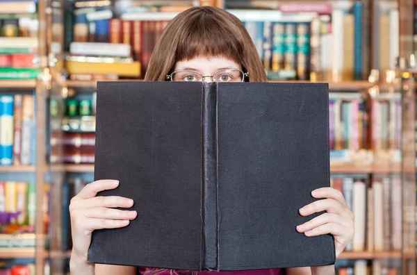 Fille lit grand livre dans la bibliothèque — Photo