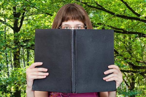 Chica mira sobre libro grande y bosques verdes —  Fotos de Stock