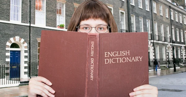 Девушка смотрит на английский словарь и улицу — стоковое фото