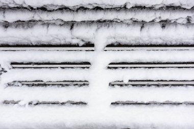 Bulutlu kış gününde, kar yağdıktan sonra şehir bahçesinde, karla kaplı ahşap bankın donmuş yüzeyi