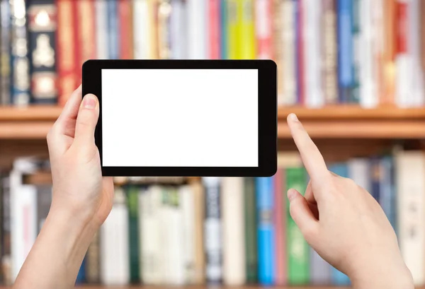Hand holds tablet pc and book shelves — Stock Photo, Image